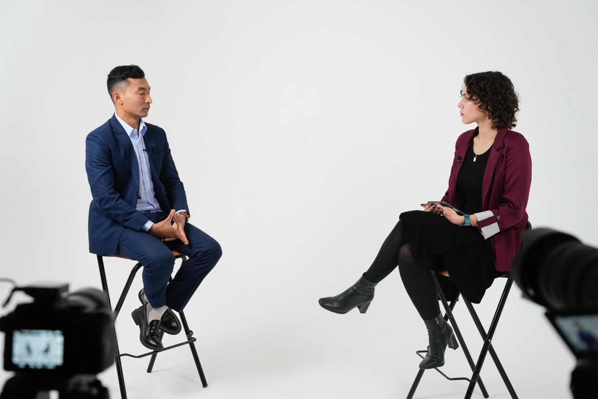 Sajan Dangol being interviewed by a woman in a maroon blazer against a white studio backdrop