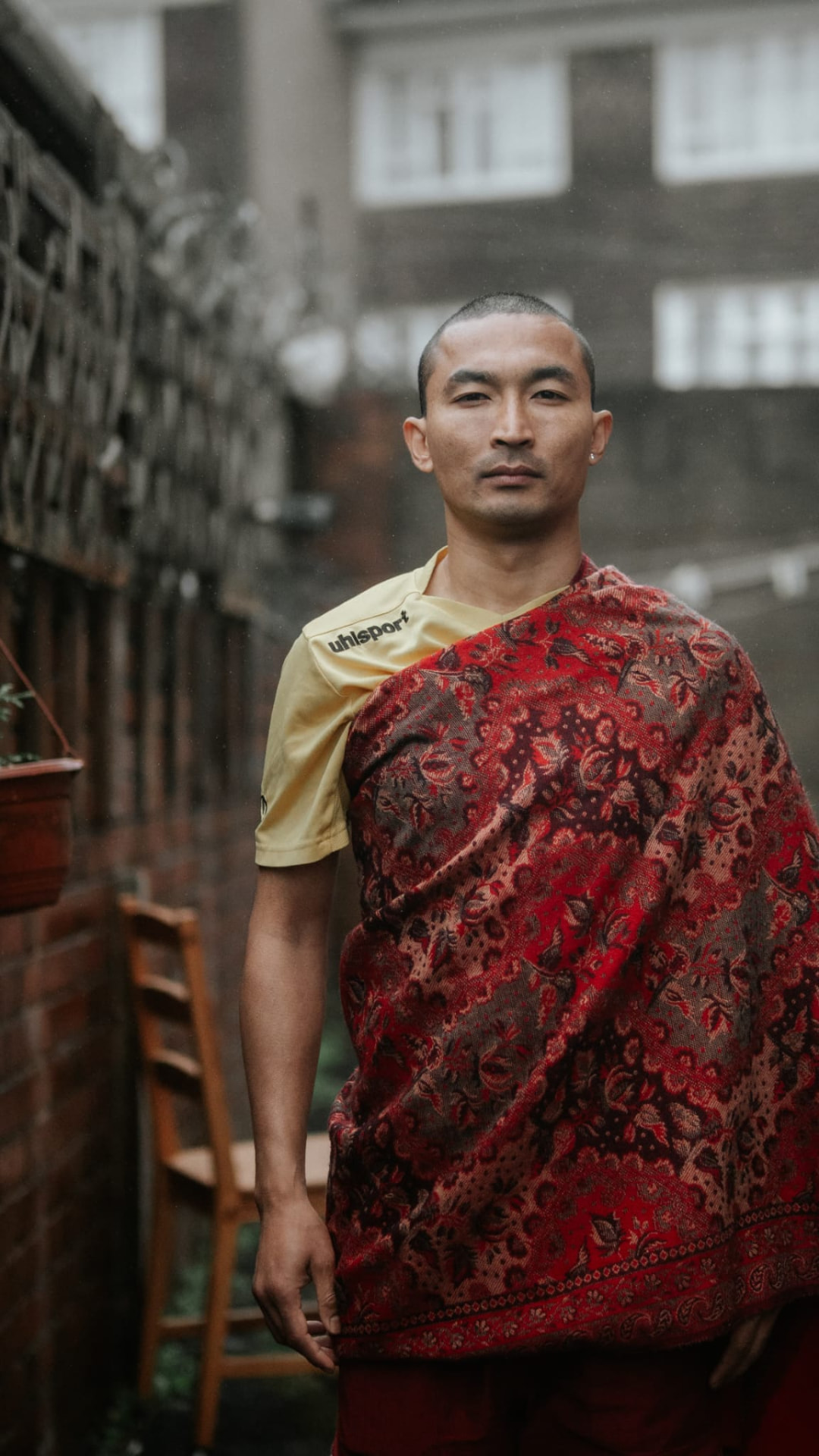Sajan Dangol standing outdoors in a yellow football shirt with a maroon patterned shawl draped across his shoulder