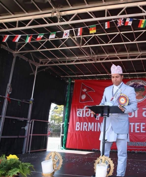 Sajan Dangol speaking at a podium on stage at a Nepali community event in Birmingham