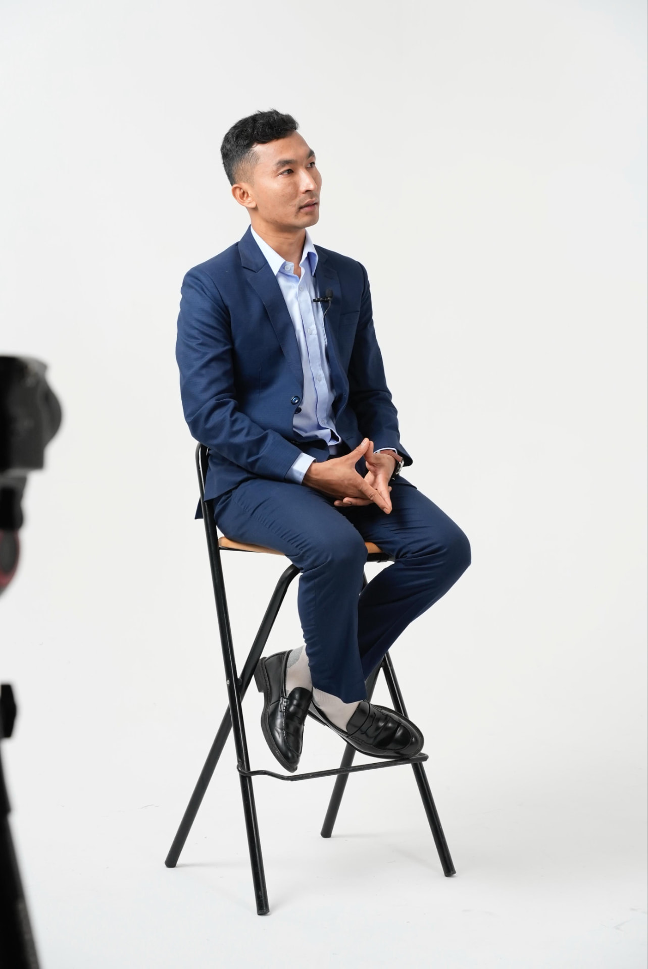 Sajan Dangol in a navy suit seated on a stool during a studio recording session