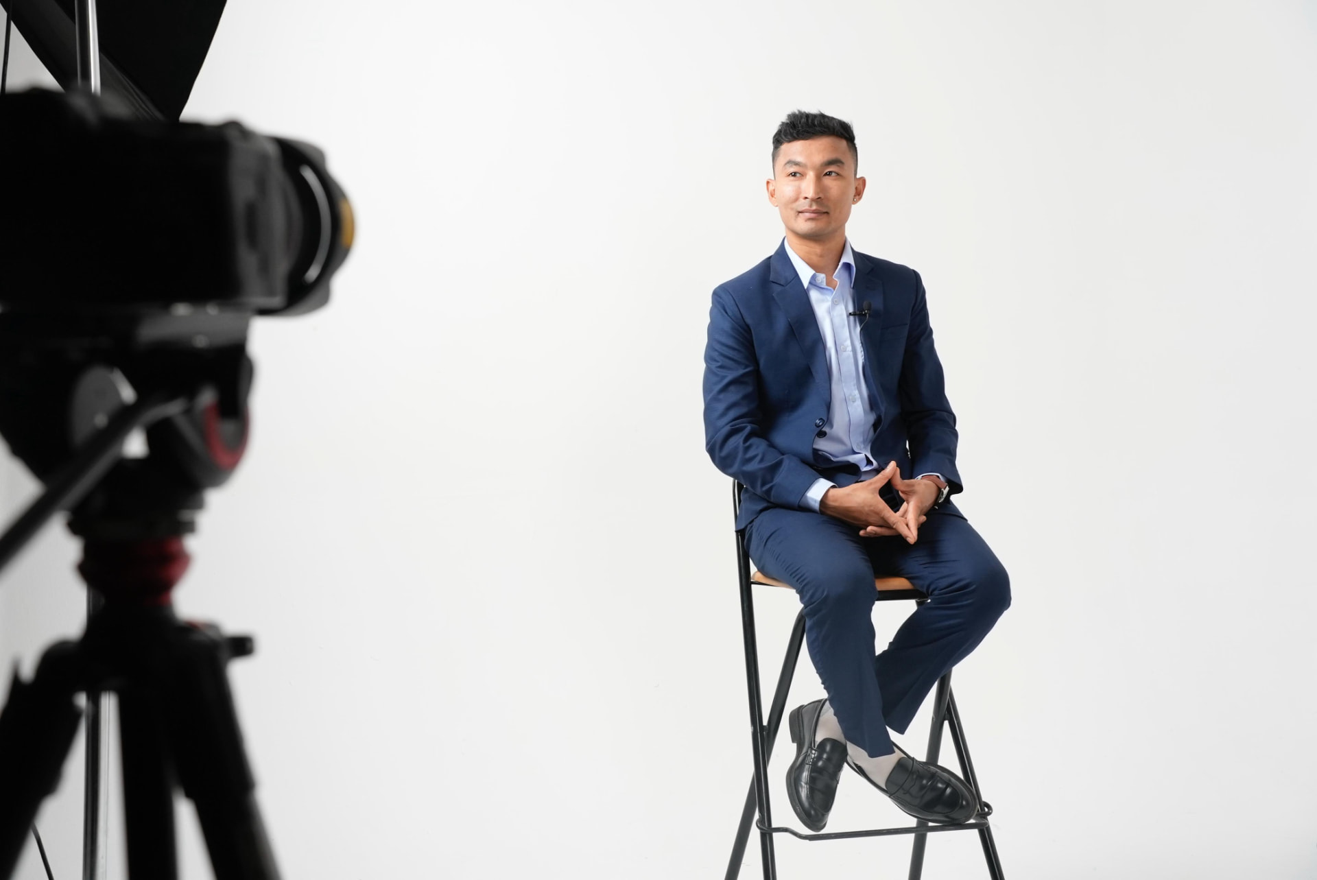 Sajan Dangol seated on a stool against a white studio backdrop during a filmed interview