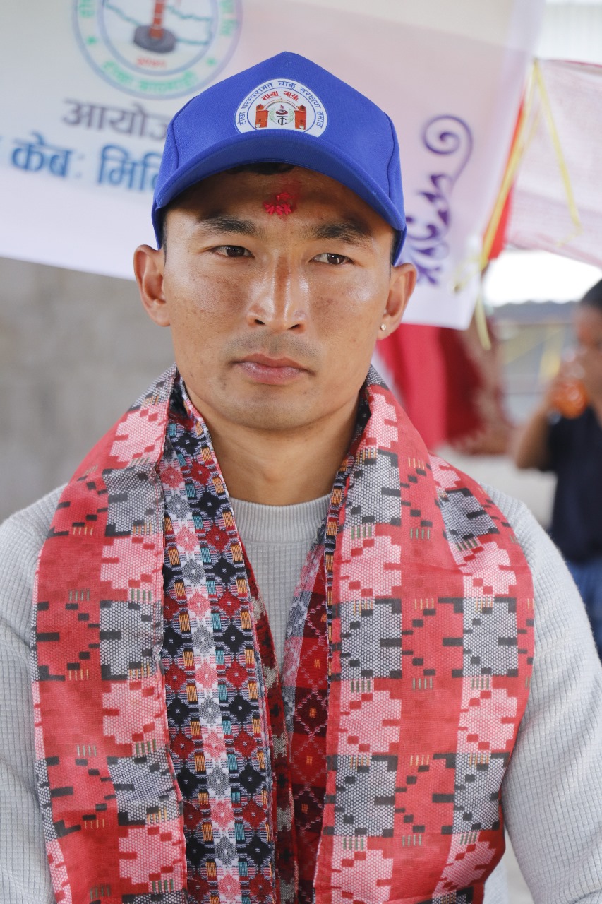 Sajan Dangol wearing a blue cap and traditional Nepali Dhaka scarf at a community event